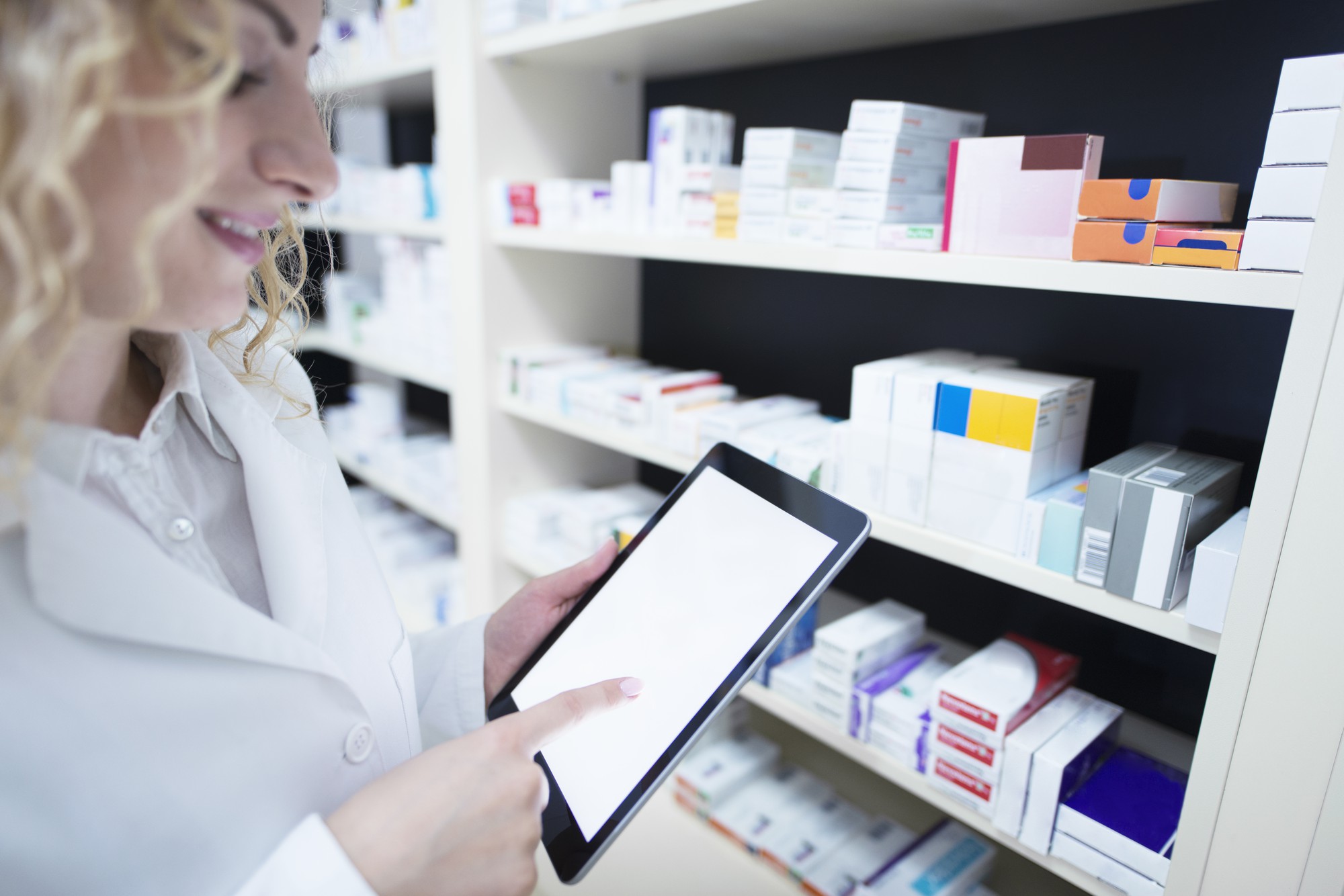 pharmacist-holding-tablet-by-shelf-full-medicine-drug-store-checking-medication-availability-specification